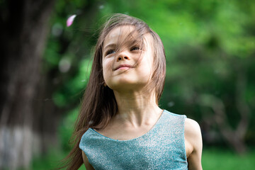 portrait of little smiling joyful girl in spring outdoors against green trees