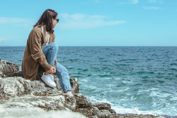 Wall Mural - woman sitting on cliff enjoying view of the sea. windy weather. sunny day