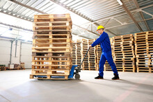 Worker Moving Wooden Pallets With Manual Forklift In Warehouse