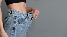 Young Fitness Woman With A Slim Waist Slender Figure Tries On Big Pants And Shows How To Lose Weight To The Camera, Close Up. Athletic Girl Lost Weight After Diet Or Exercise