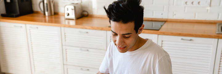 Wall Mural - Young hispanic man reading a book while having breakfast