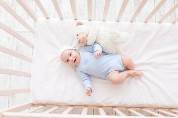 Wall Mural - baby in crib with teddy bear toy goes to bed or woke up in the morning, family and birth concept