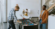 © BGStock72 - Young casual multiethnic business people playing table football and relaxing at office