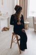 © sergiokat - Pregnant woman in black dress sitting on the chair in the studio with white background. Pregnant woman touching belly