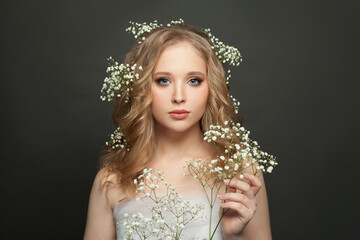 Wall Mural - Young woman portrait. Cute female model with natural makeup and healthy curly hair holding flowers