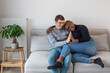 © Anna Berkut/Stocksy - happy mixed couple sitting together on couch, hug
