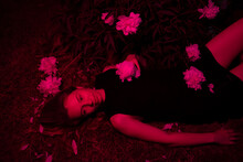 Woman Lying Among Peonies In Neon Red Light