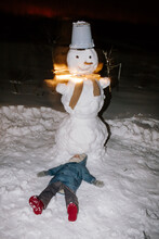 Kid In Warm Wear Lying Near Snowman