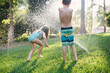 © Stacy Allen/Stocksy - Young siblings playing in a sprinkler