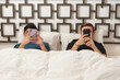 © Leire Cavia/Stocksy - Routine scene of a gay couple in bed with mobile phones