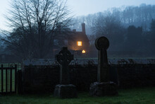 Graves In A Churchyard With A House Behind In Winter.