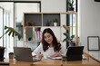 © Natee Meepian - Portrait of young asian woman sitting at her desk with laptop and taking notes. Asian businesswoman working in modern office