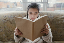 Close-up Portrait Of A Girl With Braids Reading A Book