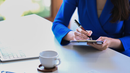 Wall Mural - Cropped shot businesswoman holding pen and writing information on notebook.