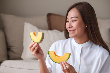 Wall Mural - Portrait image of a young woman holding and eating two pieces of Cantaloupe melon