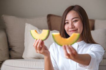 Wall Mural - Portrait image of a young woman holding and eating two pieces of Cantaloupe melon