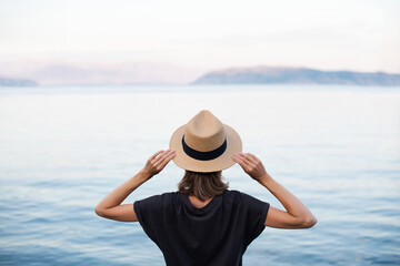 Wall Mural - Young woman enjoy life by the sea. Beautiful girl wearing hat on beach at sunset. Enjoying life, summer fun, relaxation and travel lifestyle concept