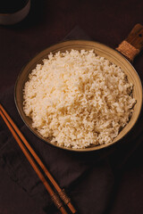 A plate of boiled rice, with wooden sticks, on a brown background, no people, selective focus, toned.