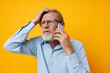 © Tatiana - Portrait elderly man in a blue shirt and glasses talking on the phone yellow background