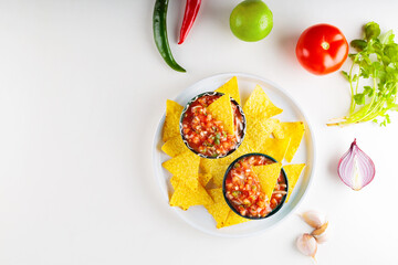 Wall Mural - Salsa sauce and nacho chips on white plate. Mexican homemade salsa dip and ingredients on a white background. Copy space. Top view