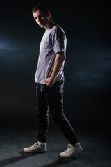 Sticker - Handsome young man wearing a gray t-shirt and black pants poses on black background in a studio