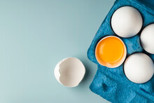 White Chicken Eggs In Eco-packaging On A Blue Background. Broken Egg With Yolk In The Shell. Farm Natural Products. Top View. Copy Space