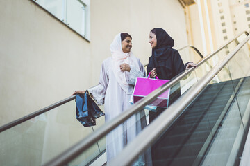 Wall Mural - Two arabian girls spending time together outdoor making activities. Young women making shopping in Dubai