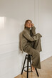 © Look! - Full-length, happy young european lady, laughing heartily, sits on chair in front of white wall. Girl with gathered blond hair in glasses and suit, barefoot. Leisure lifestyle and beauty concept.