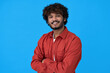 © insta_photos - Smiling young curly indian cool guy standing isolated on blue background. Happy ethnic stylish millennial confident man looking at camera posing with arms crossed for portrait.