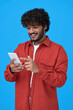 © insta_photos - Happy indian young man using cell phone isolated on blue background. Smiling ethnic guy holding smartphone playing game in digital app, dating online, buying online in e commerce store, vertical.