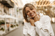 © Look! - Close up portrait caucasian young happy woman with fresh and clean skin stands outside. Smiling blonde holds collar of white sweatshirt. Lifestyle, female beauty concept