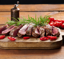 Wall Mural - roasted piece of beef ribeye cut into pieces on a vintage brown chopping board, rare doneness. Delicious steak, close up