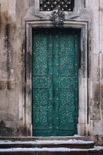 The Old Vintage Green Metal Door On The Facade Of The Baroque Dominican Cathedral In Lviv Is Decorated With Decorative Forged Flowers. Snow Lies On The Stairs Above The Doorway.