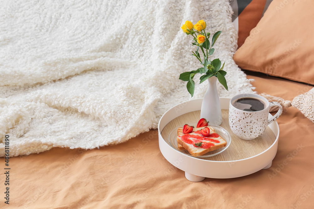 Tray with tasty breakfast and vase with flowers on comfortable bed