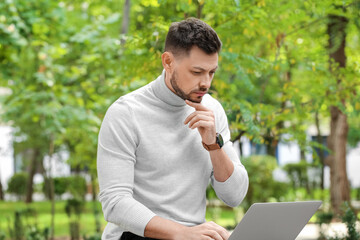 Poster - Stylish businessman working with laptop on bench in park