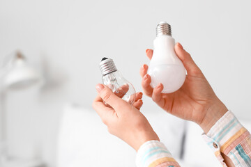 Wall Mural - Woman holding different light bulbs in bedroom, closeup