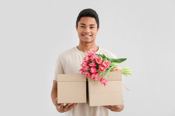 Canvas Print - African-American man with gift boxes and bouquet of tulips on light background. International Women's Day celebration