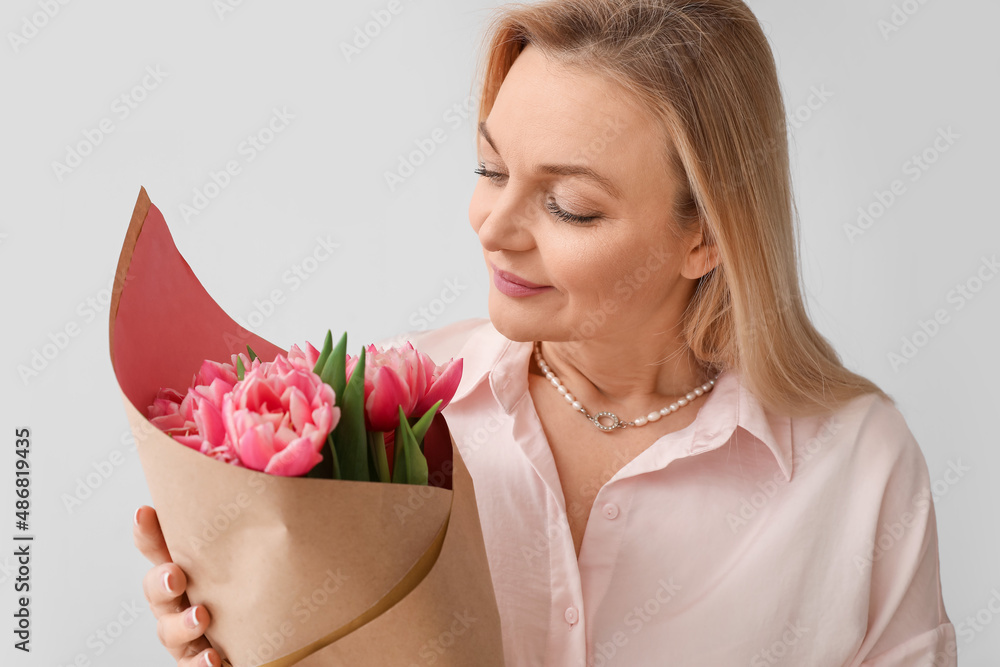 Woman with bouquet of tulips on light background. International Women's Day celebration