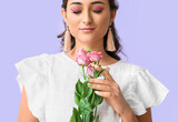 Young woman with creative makeup and closed eyes holding eustoma flowers on violet background. International Women's Day