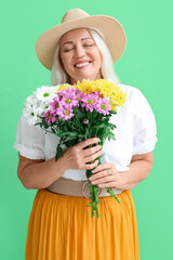 Poster - Happy mature woman holding bouquet of beautiful flowers on green background. International Women's Day celebration