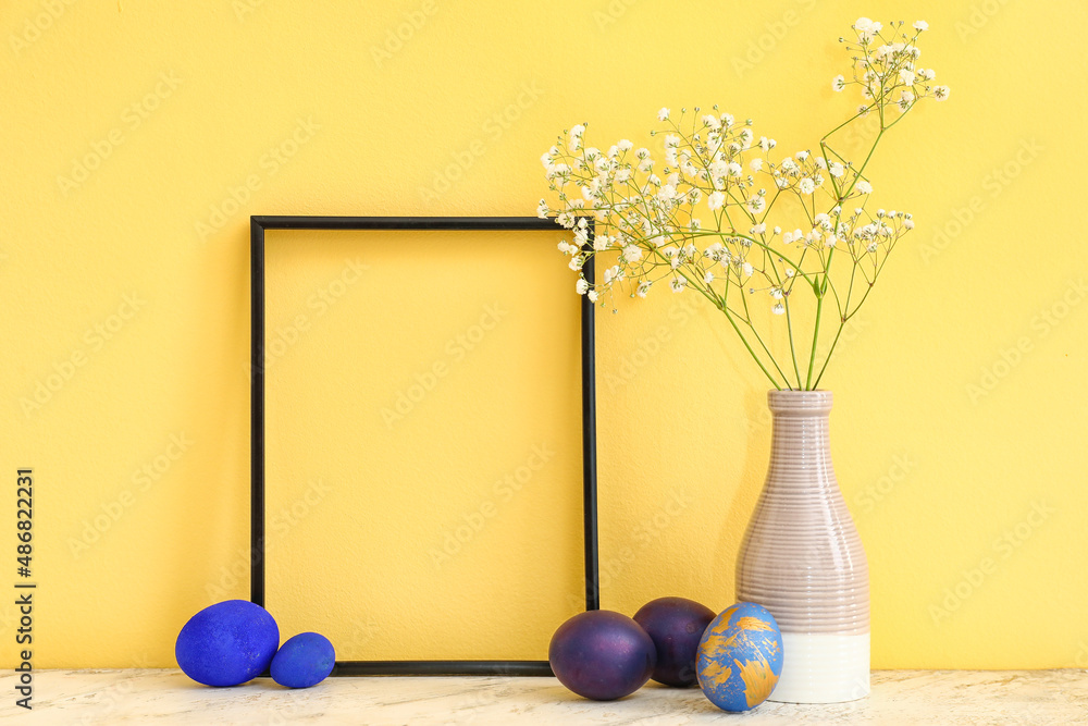 Empty picture frame, vase with gypsophila flowers and Easter eggs on color background