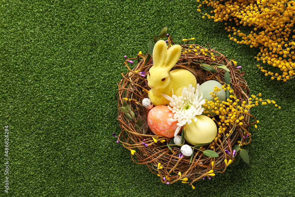 Nest with painted Easter eggs, bunny and flowers on green background