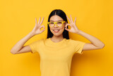 Fototapeta Do pokoju - Charming young Asian woman in glasses gesturing with hands copy-space yellow background unaltered