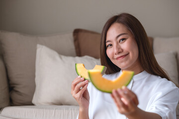 Wall Mural - Portrait image of a young woman holding and eating two pieces of Cantaloupe melon