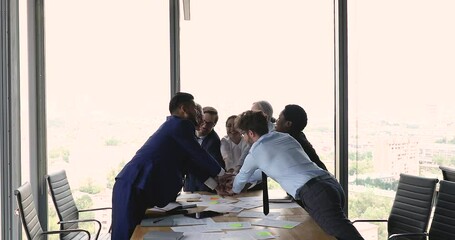 Wall Mural - Motivated happy multiracial teammates of diverse generation gender engaged in teambuilding activity stack hands above conference table. Joyful partners feel corporate spirit celebrate business success