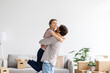 © Prostock-studio - Satisfied european young husband lifts and hugs his wife in room interior have fun together
