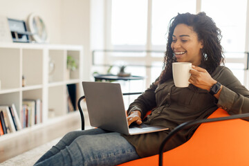 Canvas Print - Smiling black lady watching video on computer, drinking hot coffee