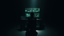 Zoom out view of unrecognizable man in mask turning to desk and starting to hack database on computers in dark room