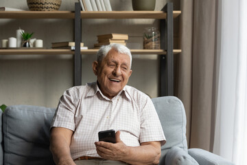 happy joyful older 80s man holding, using online ecommerce app on mobile phone, resting on sofa at h