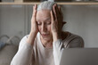 Exhausted frustrated mature retired woman touching head with closed eyes at laptop computer, suffering from headache, dry eyes problem, getting bad news from internet, online chat, feeling upset